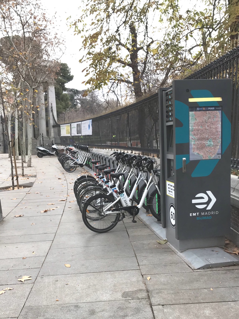 En elbil med to cykler monteret bagpå, parkeret ved en ladestander.
